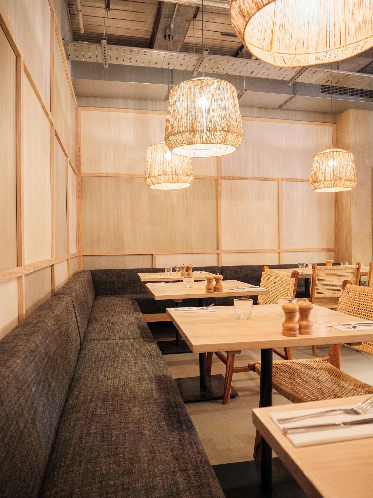 Modern Caravan Canary Wharf restaurant interior with wooden tables, chairs, and wicker pendant lights.