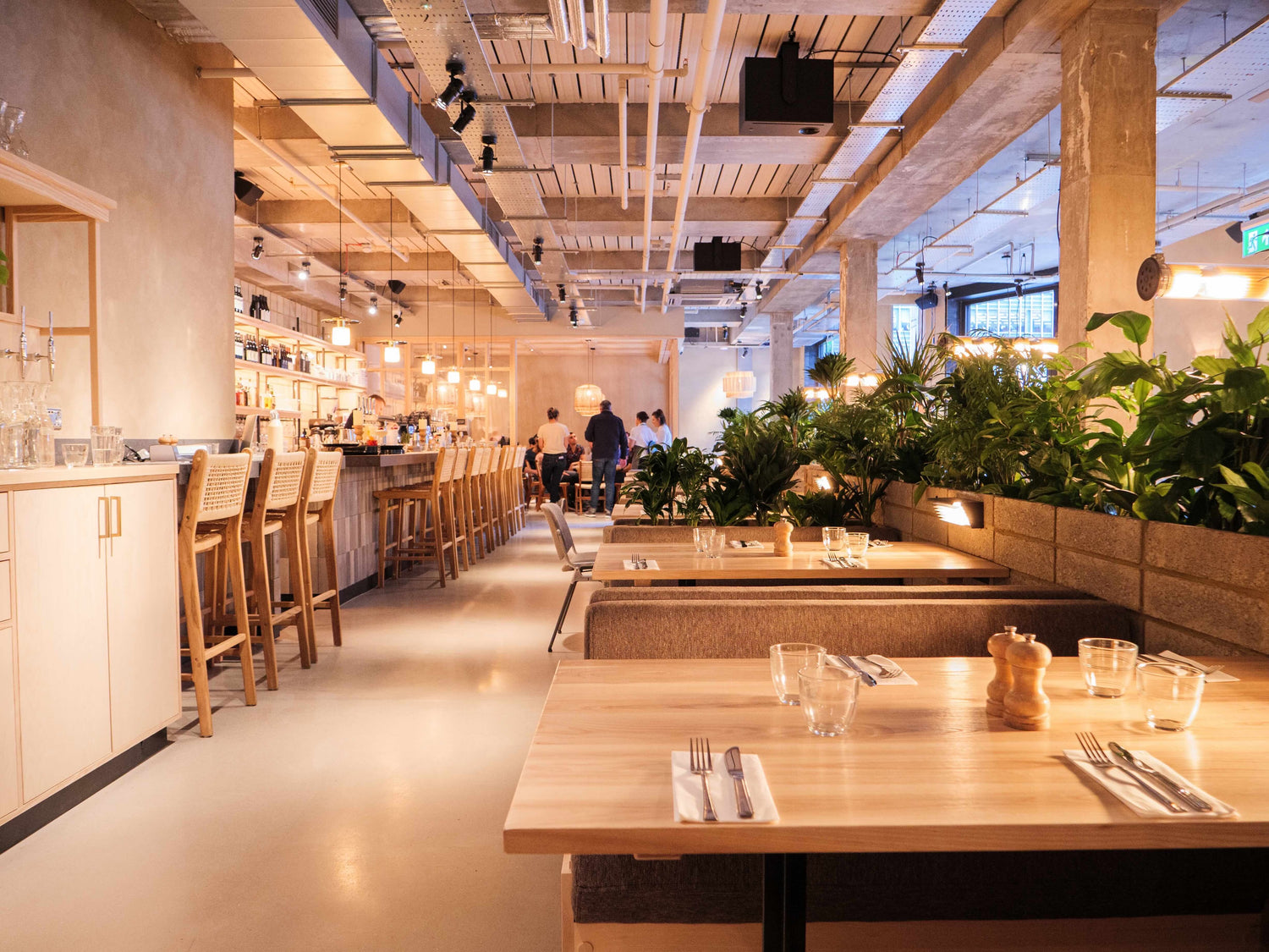 Modern Caravan Canary Wharf restaurant interior with wooden tables, chairs, and plants.