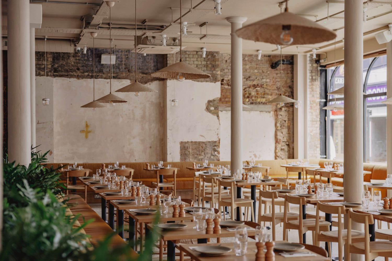 Empty restaurant with wooden tables and chairs, exposed brick walls, and pendant lights.