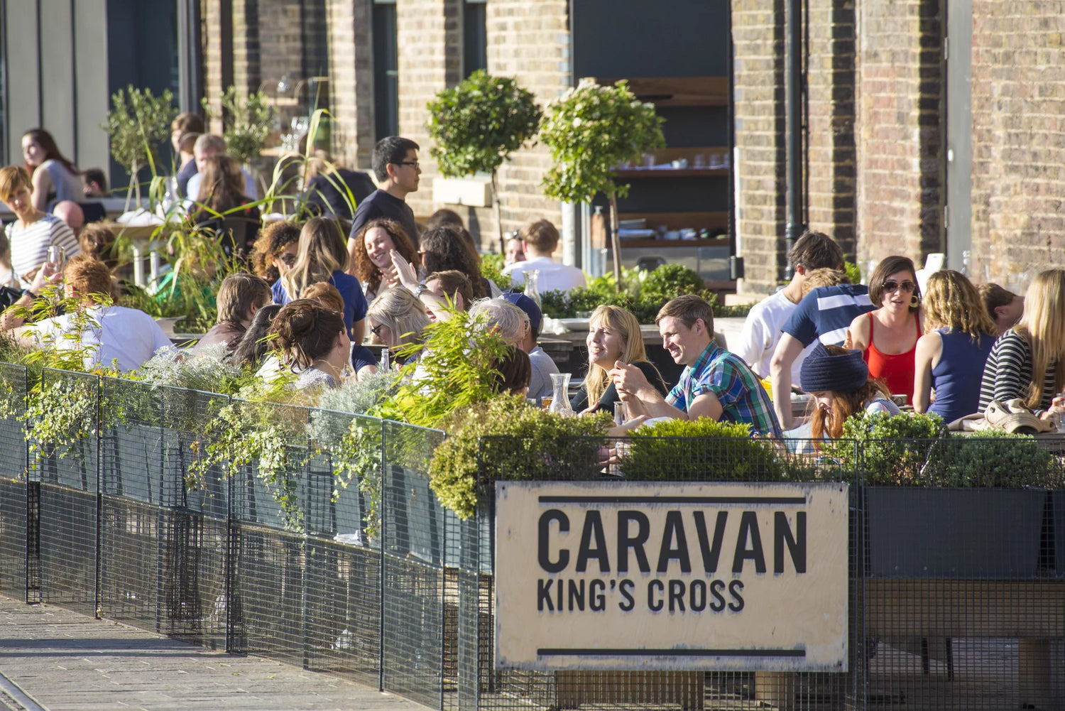 People enjoying outdoor seating at a restaurant with a 'Caravan King's Cross' sign.